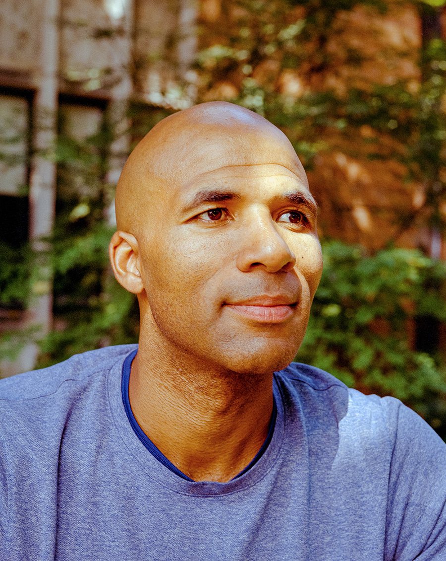 Headshot of Akwasi Owusu-Bempah in a blue shirt, with trees and shrubs out of focus in the background