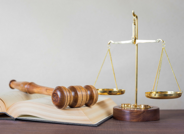 A wooden gavel on top of a book and beside a set of brass scales.